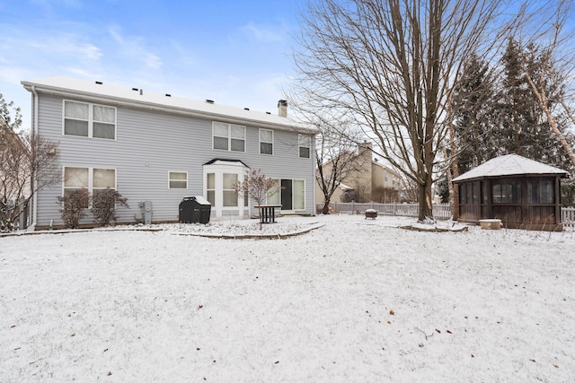 snow covered rear of property with a garage, a sunroom, a chimney, fence, and a gazebo