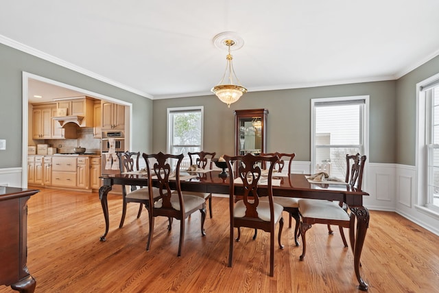 dining space with light wood-type flooring, a wainscoted wall, and ornamental molding