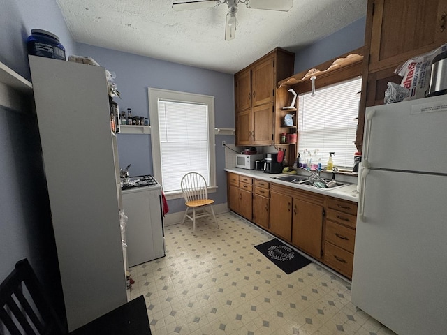 kitchen with a textured ceiling, ceiling fan, white appliances, and sink