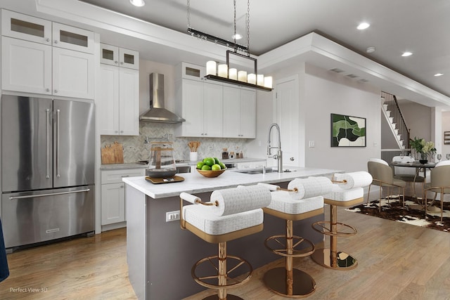 kitchen featuring a center island with sink, wall chimney range hood, sink, light hardwood / wood-style flooring, and appliances with stainless steel finishes