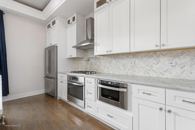 kitchen with wall chimney range hood, light stone countertops, dark hardwood / wood-style flooring, white cabinetry, and stainless steel appliances