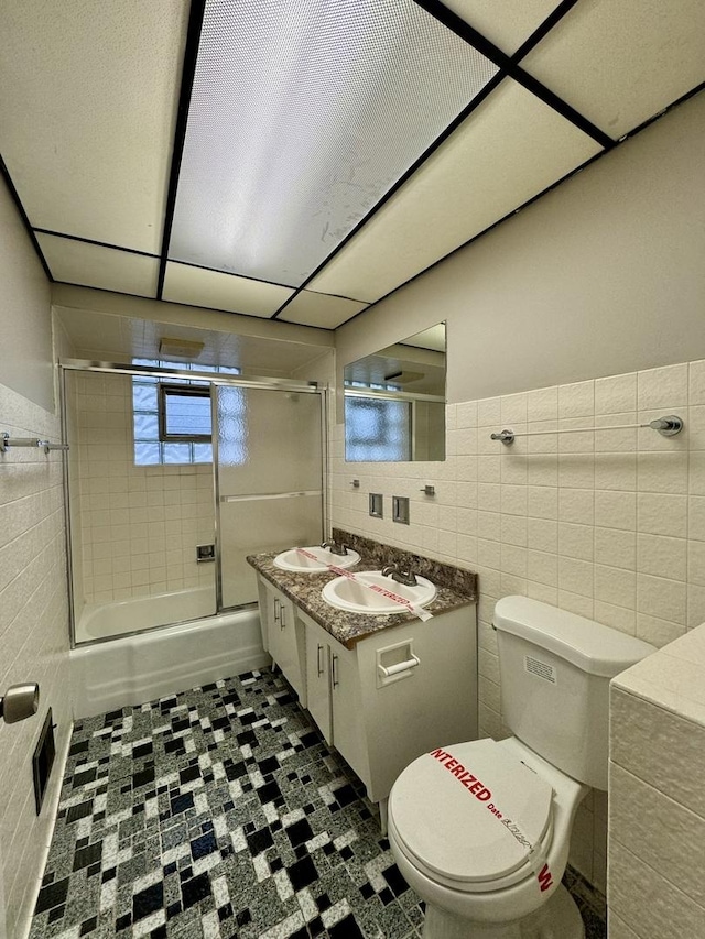 full bathroom featuring toilet, combined bath / shower with glass door, tile walls, and vanity