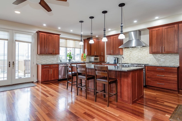 kitchen featuring light stone countertops, wall chimney exhaust hood, stainless steel appliances, a kitchen island, and hardwood / wood-style flooring