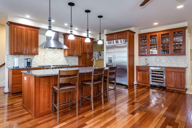 kitchen with stainless steel appliances, beverage cooler, wall chimney range hood, pendant lighting, and dark hardwood / wood-style floors