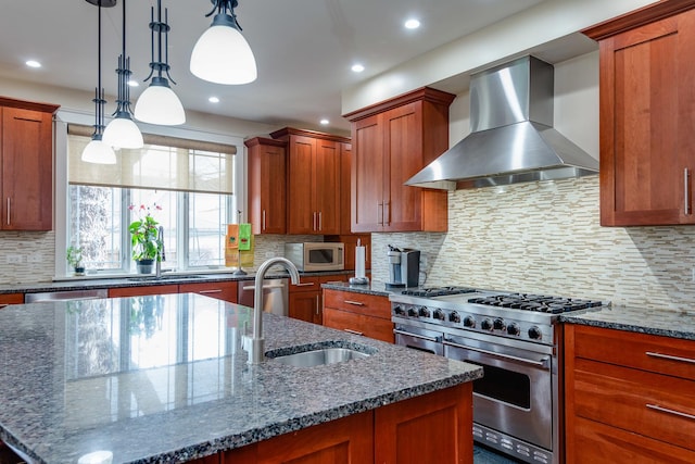 kitchen with sink, wall chimney exhaust hood, dark stone counters, decorative light fixtures, and appliances with stainless steel finishes