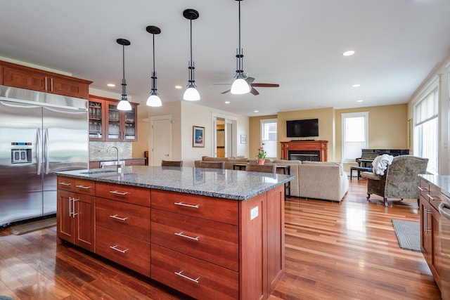 kitchen with a kitchen island with sink, stainless steel built in fridge, sink, hardwood / wood-style flooring, and decorative backsplash