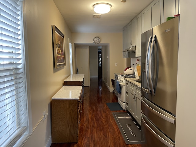 kitchen with gray cabinetry, dark wood-type flooring, stainless steel refrigerator with ice dispenser, light stone countertops, and white range with gas stovetop