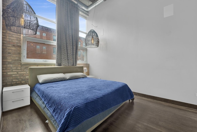 bedroom with brick wall and dark hardwood / wood-style flooring