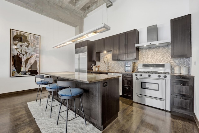 kitchen featuring a center island, dark wood-type flooring, wall chimney range hood, stainless steel appliances, and a breakfast bar area