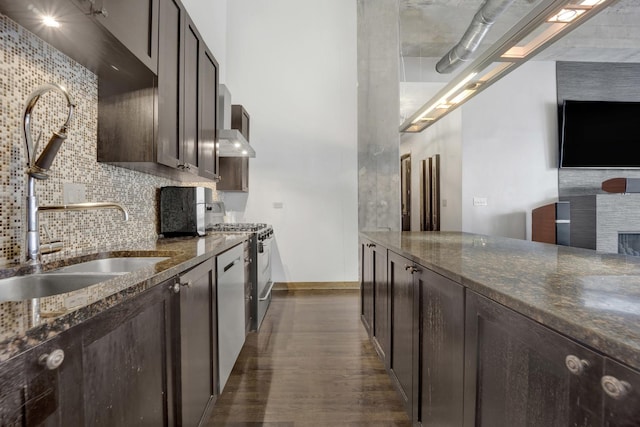 kitchen with sink, backsplash, dark stone countertops, and stainless steel gas range oven