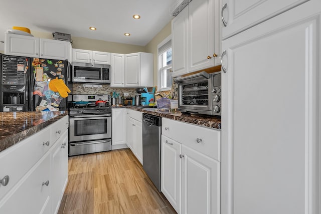 kitchen with stainless steel appliances, white cabinets, decorative backsplash, dark stone counters, and light wood-type flooring