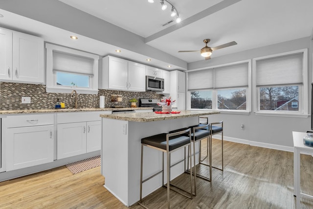 kitchen with backsplash, stainless steel appliances, a center island, light stone counters, and white cabinets