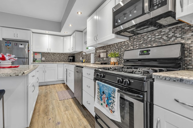 kitchen featuring sink, white cabinetry, tasteful backsplash, light wood-type flooring, and appliances with stainless steel finishes