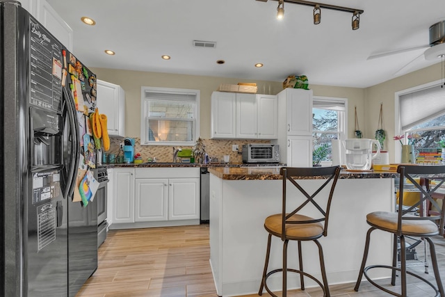 kitchen with white cabinetry, backsplash, a breakfast bar, and black fridge