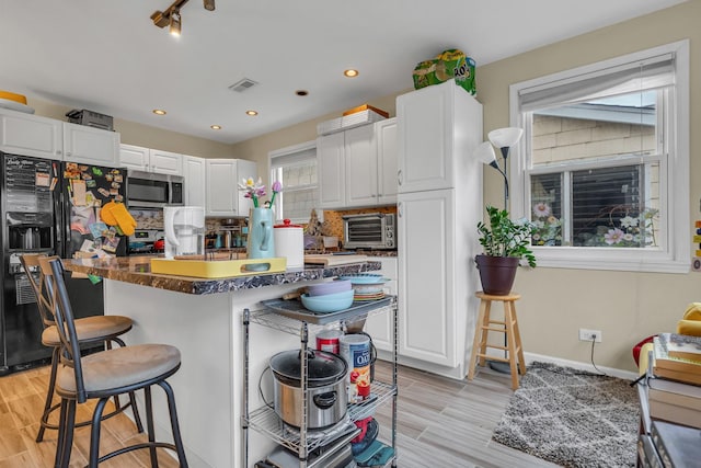 kitchen featuring black refrigerator with ice dispenser, white cabinets, and a kitchen bar