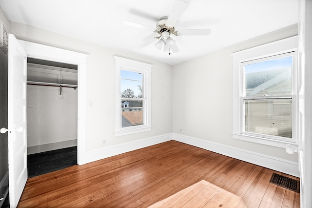 unfurnished bedroom featuring multiple windows, ceiling fan, a closet, and hardwood / wood-style flooring