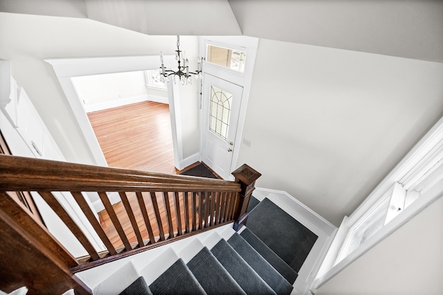 stairs with wood-type flooring, an inviting chandelier, and lofted ceiling