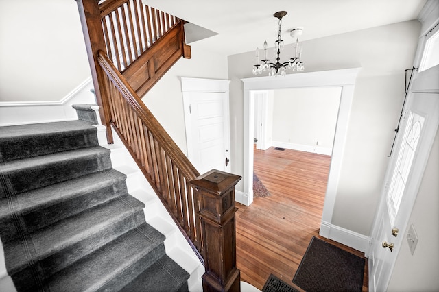 stairs featuring wood-type flooring and an inviting chandelier