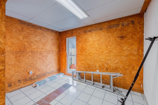 unfurnished room featuring a drop ceiling, light tile patterned flooring, and wooden walls