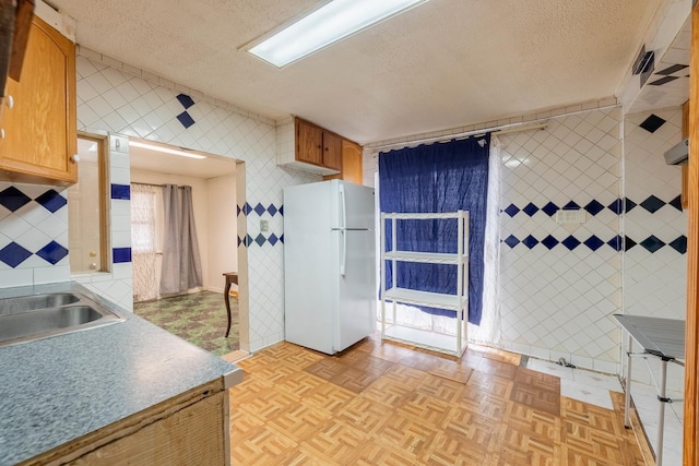 kitchen with a textured ceiling, light parquet flooring, white fridge, and tile walls