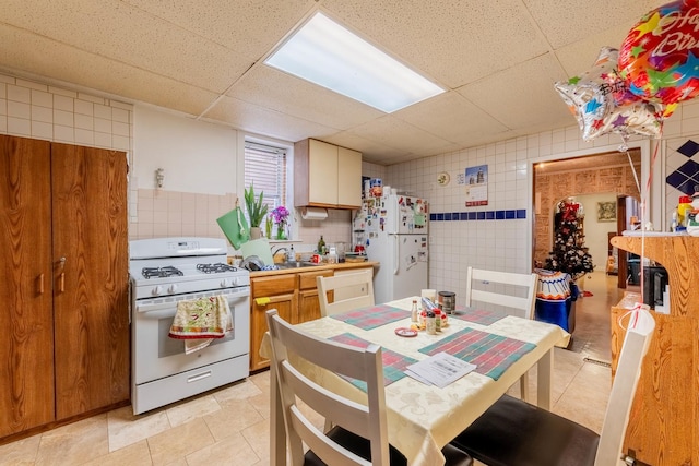 kitchen featuring a paneled ceiling, light tile patterned flooring, white appliances, and tile walls