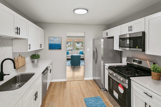 kitchen featuring sink, stainless steel appliances, decorative backsplash, white cabinets, and light wood-type flooring