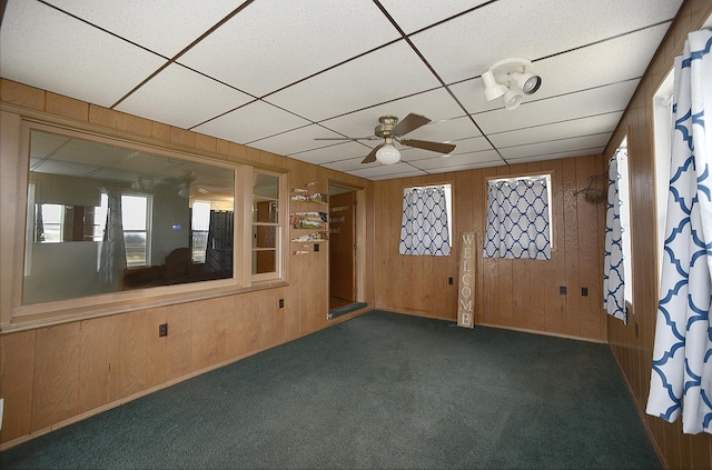 carpeted empty room featuring a paneled ceiling, ceiling fan, and wood walls