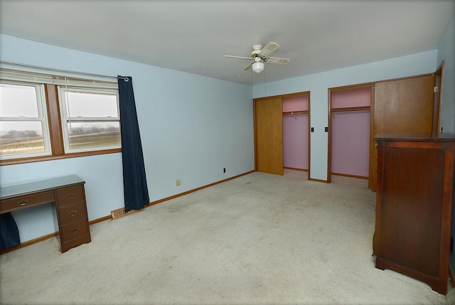 unfurnished bedroom featuring ceiling fan, light colored carpet, and two closets