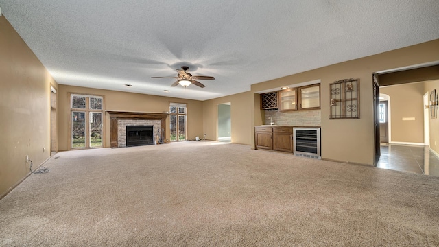 2239 Pine Bluff Dr, Dixon, IL 61021 - unfurnished living room featuring wine cooler, ceiling fan, a brick fireplace, carpet floors, and a dry bar