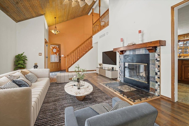 living room featuring a stone fireplace, dark hardwood / wood-style flooring, a towering ceiling, and wooden ceiling