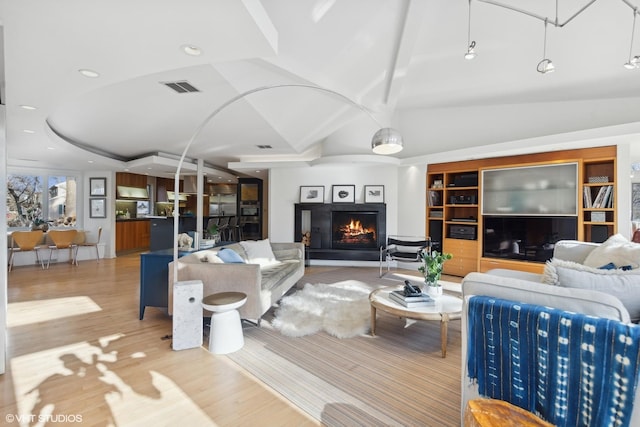 living room featuring built in shelves, light hardwood / wood-style flooring, and vaulted ceiling