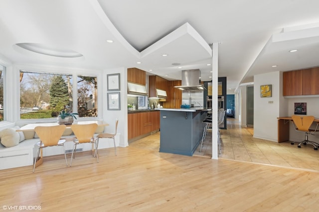 kitchen featuring a center island, a kitchen breakfast bar, light hardwood / wood-style flooring, island exhaust hood, and a tray ceiling