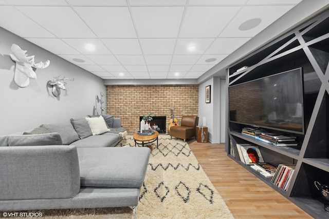 living room featuring built in shelves, a paneled ceiling, hardwood / wood-style floors, and a brick fireplace