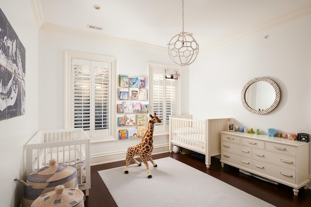 bedroom featuring a nursery area, visible vents, dark wood-style flooring, and ornamental molding