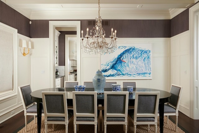 dining room featuring dark wood-style flooring, ornamental molding, a decorative wall, and a notable chandelier