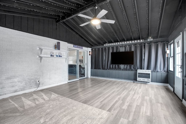 unfurnished living room featuring ceiling fan, brick wall, heating unit, hardwood / wood-style floors, and vaulted ceiling