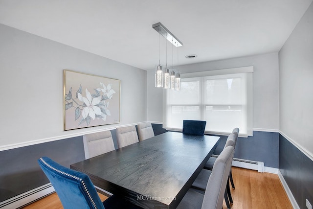 dining space featuring wood-type flooring, a baseboard heating unit, and a notable chandelier