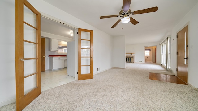 unfurnished living room with ceiling fan, french doors, and light carpet