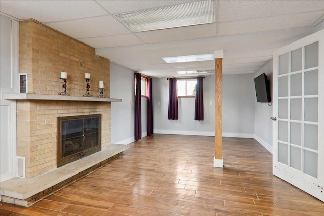 unfurnished living room with a paneled ceiling, a brick fireplace, and hardwood / wood-style flooring