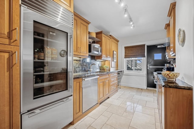 kitchen with tasteful backsplash, dark stone countertops, a sink, stainless steel appliances, and baseboards