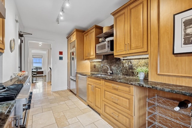 kitchen with appliances with stainless steel finishes, dark stone countertops, brown cabinets, decorative backsplash, and a sink