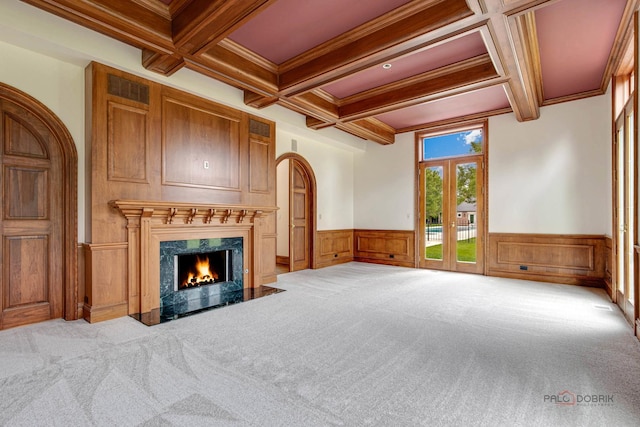 unfurnished living room featuring coffered ceiling, a premium fireplace, light carpet, and crown molding