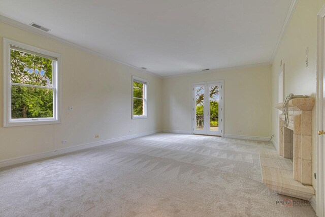 unfurnished living room with a tile fireplace, french doors, crown molding, and light carpet