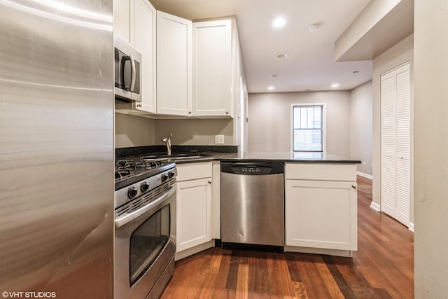 kitchen with white cabinets, sink, kitchen peninsula, dark hardwood / wood-style flooring, and stainless steel appliances