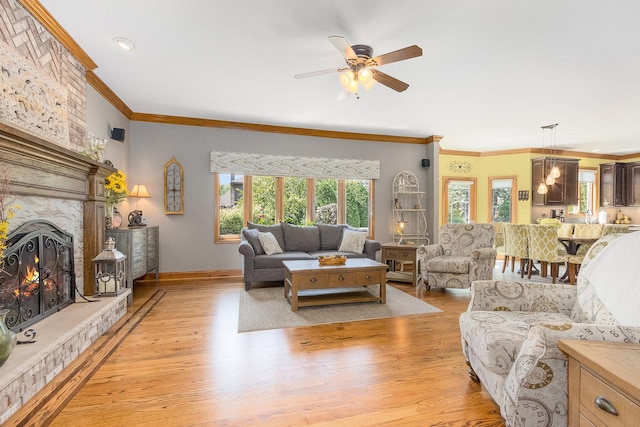 living room featuring a fireplace, crown molding, light hardwood / wood-style flooring, and ceiling fan with notable chandelier