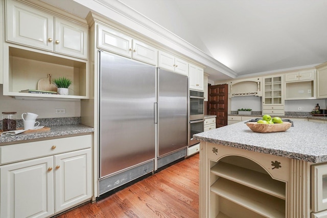 kitchen featuring light wood-type flooring, cream cabinets, appliances with stainless steel finishes, and vaulted ceiling