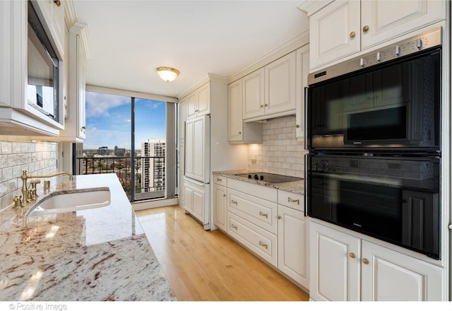 kitchen with light hardwood / wood-style floors, multiple ovens, black electric cooktop, light stone counters, and sink