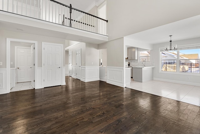 unfurnished living room featuring light hardwood / wood-style floors, sink, a towering ceiling, and a chandelier