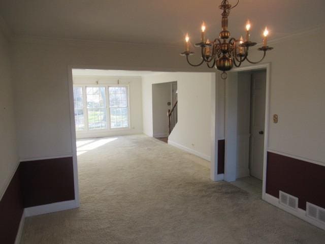 spare room with carpet floors, crown molding, and a chandelier