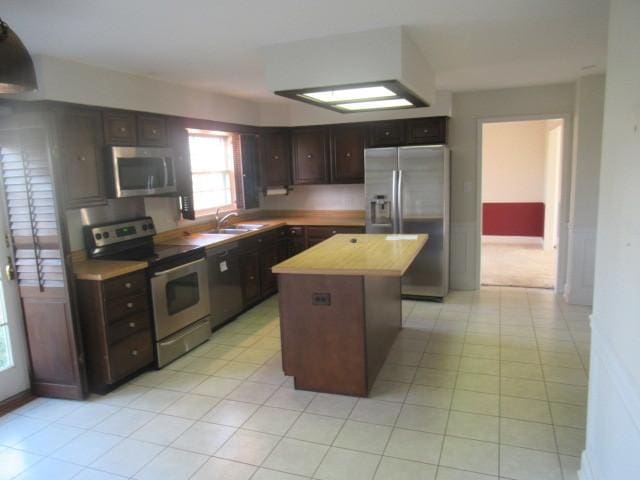 kitchen with a center island, sink, light tile patterned floors, appliances with stainless steel finishes, and dark brown cabinetry